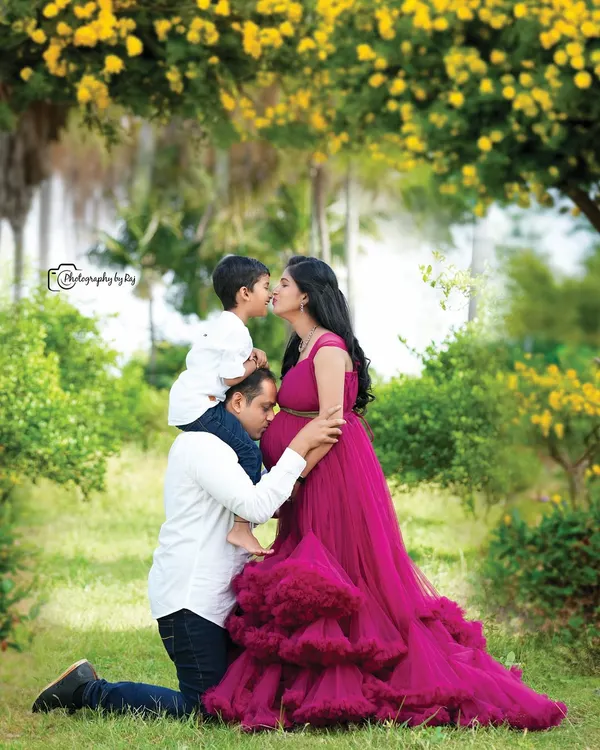 A beautiful family moment captured in our private garden. The father-to-be kneels to kiss the baby bump while their older son, perched on his shoulders, gives his mother a sweet kiss. This image showcases our elegant couture gowns and ability to capture genuine, loving interactions.