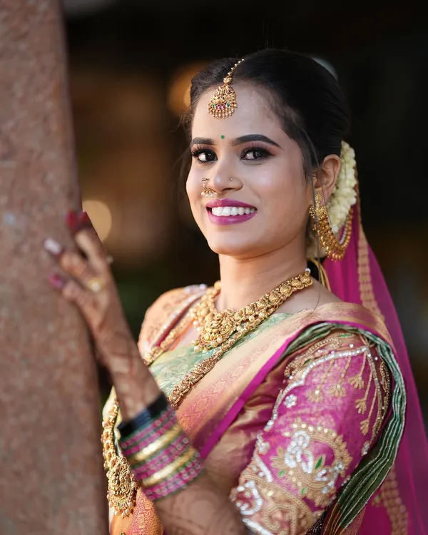 A radiant close-up of a South Indian bride, showcasing her beautiful smile, intricate gold jewelry, and the detailed embroidery on her wedding saree.