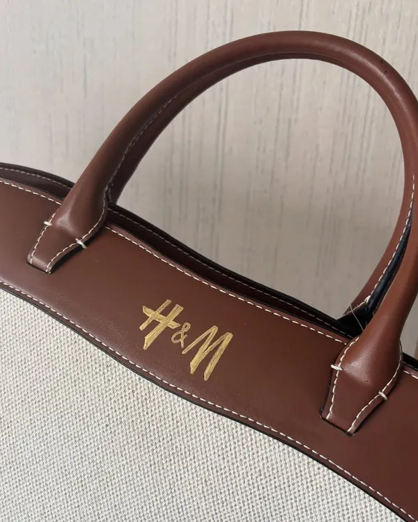 Calligraphy on leather requires a slow, steady hand. Here, I personalized an H&M canvas tote bag by painting the logo and a name on the leather handle, sealing it with a fixative to ensure it lasts.