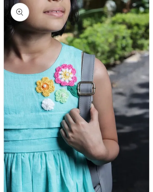 A beautiful close-up of a floral arrangement patch on a girl's aqua blue dress. The different flower sizes and colors, some with pearl centers, create a lovely bouquet effect.
