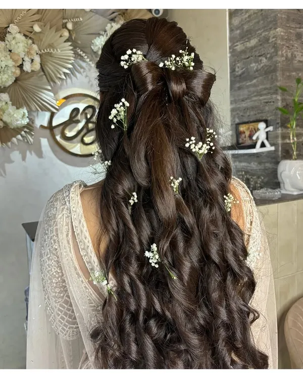 A beautiful half-up hairstyle featuring a bow made of hair and loose, romantic curls. We added delicate baby's breath for a whimsical and feminine touch.