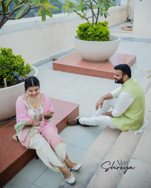 A relaxed moment during a Mehendi ceremony. The couple is sitting together on a rooftop, enjoying the quiet moments before the big celebrations begin.