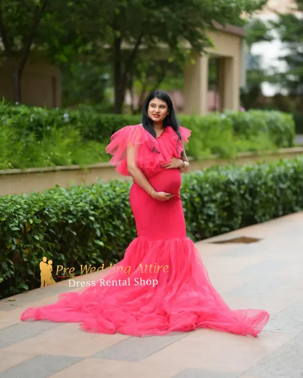 This vibrant red mermaid gown features a ruffled neckline and a sheer tulle train, creating a bold and stylish look. It's perfect for an outdoor maternity shoot in a modern park or garden setting.