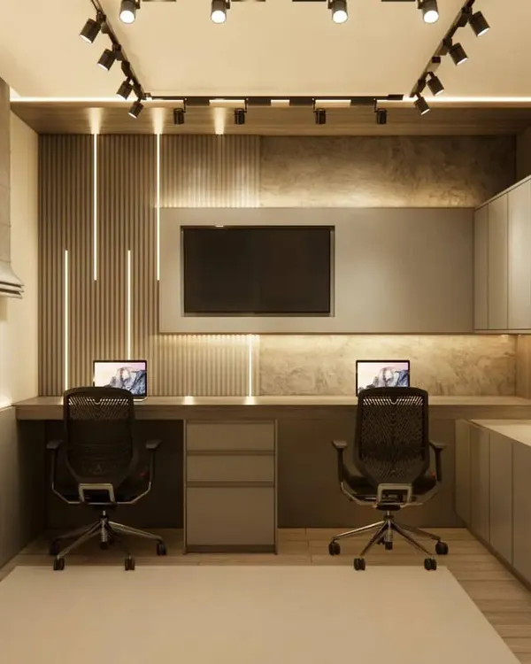 A highly functional home office designed for two people. This setup includes a long shared desk, ergonomic chairs, and ample overhead and lower cabinet storage, all illuminated by modern track lighting.