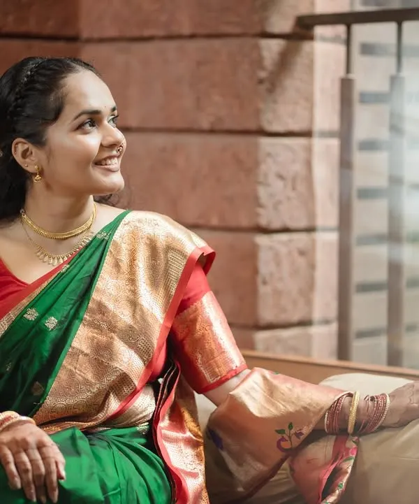 A beautiful bridal portrait capturing a moment of quiet reflection, with soft window light highlighting her joyful expression and traditional green saree.