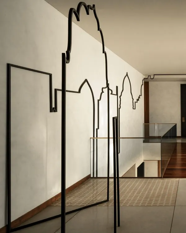 A closer view of the "Continuous Fragments" installation, where the black metal line travels from a wall-mounted piece to a freestanding element, blurring the line between two-dimensional drawing and three-dimensional sculpture.