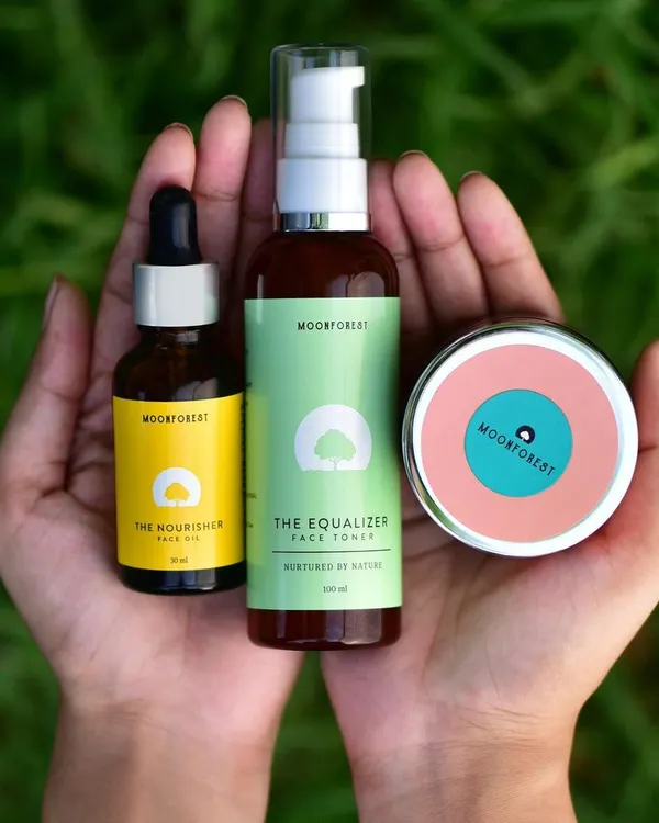 A lifestyle shot showing the Moon Forest skincare line held in hands against a natural green background. This connects the products to nature and personal care.