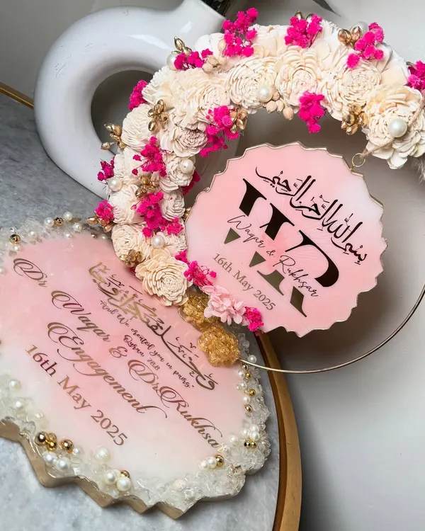 A beautiful pink and white resin ring platter for an engagement. This set includes a main tray for the ceremony and a matching hanging piece with the couple's initials, all decorated with sola wood flowers and pops of bright pink.