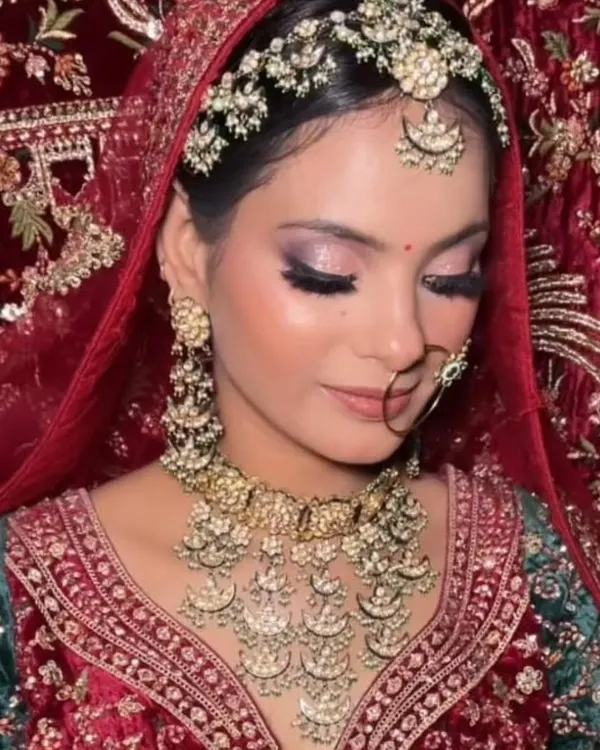 A beautiful close-up showcasing a soft glam bridal makeup look, complemented by our intricate Polki matha patti and layered necklace set against a rich red and green velvet lehenga.