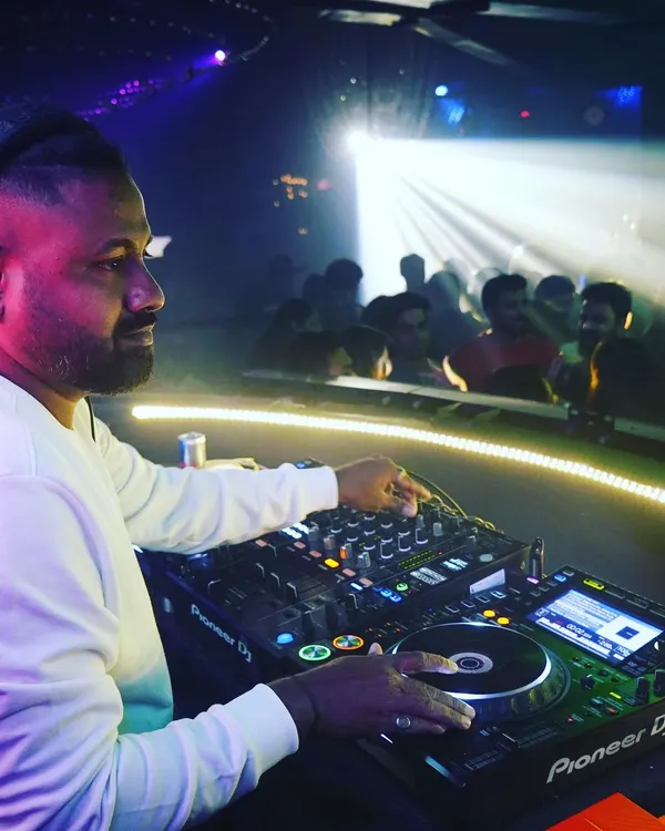 A side profile shot of me at the decks at Cavalry Lounge, with the crowd visible in the background. The spotlight catches the intensity and focus required to manage the music and the room.