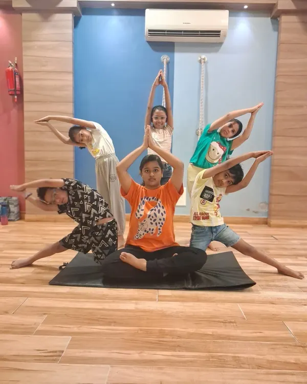 We believe fitness is about teamwork and fun. Here, our young students from a summer camp work together to create a group yoga pose, building strength, balance, and friendship all at once.