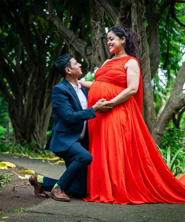 A classic pose that is always full of emotion. The father-to-be kneels to connect with his baby, while the mother-to-be, in a stunning red gown, looks on with love. This was taken in a beautiful green park, adding to the romantic feel.