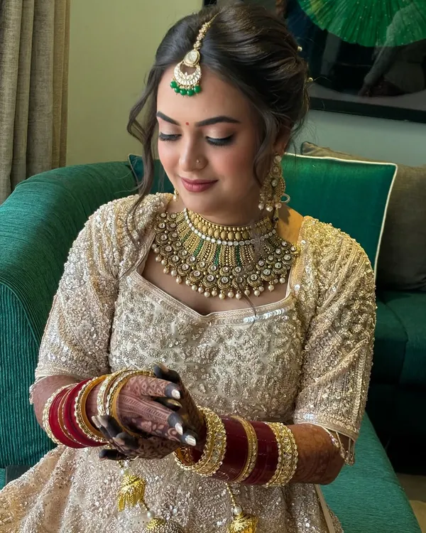 A dreamy bridal look featuring a soft, romantic updo with delicate twists and face-framing tendrils. This hairstyle perfectly complements her intricate lehenga and jewelry.