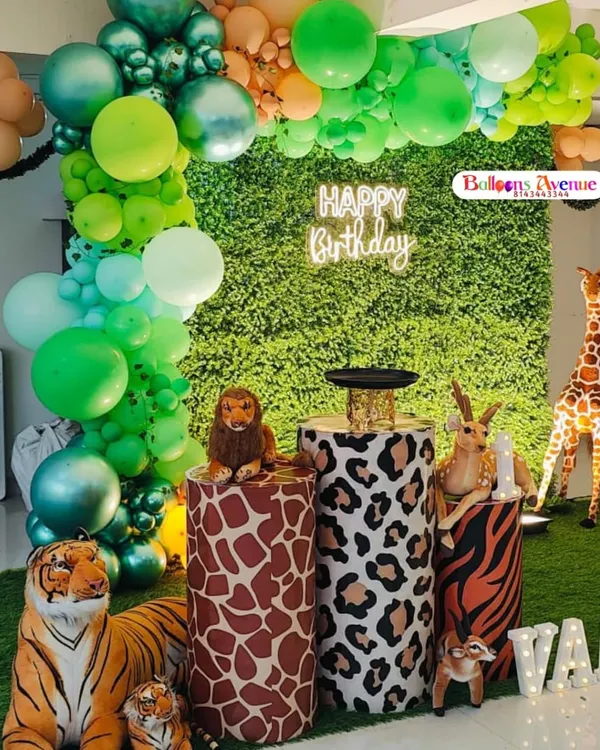 A vibrant jungle safari theme featuring a green foliage wall, a "Happy Birthday" neon sign, and animal-print pedestals for the cake. The setup is complete with life-like tiger, lion, and deer props.