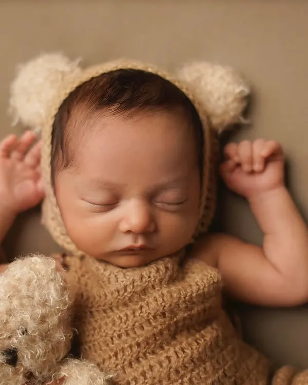 A close-up of a sleeping newborn dressed as a tiny bear, complete with a matching teddy. This pose highlights the peacefulness of a newborn, perfect for a classic infant portrait.