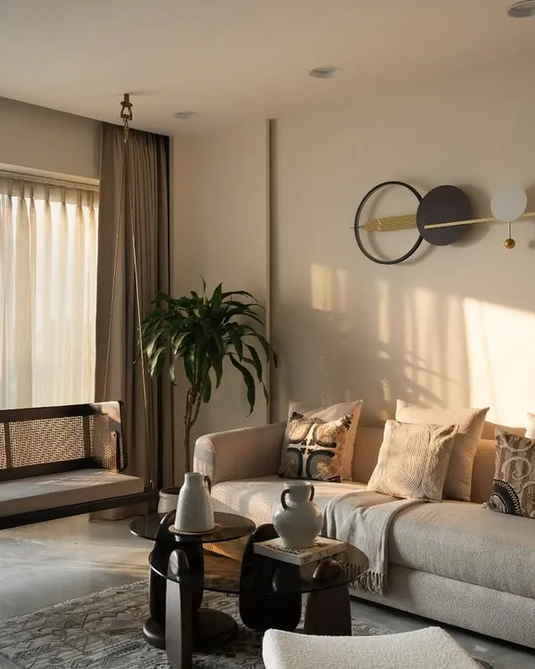 Golden hour in Project 'Sukoon'. This living room is a perfect example of warm minimalism, where soft neutrals, a comfortable boucle sofa, and a handcrafted cane swing come together to create a space of pure tranquility.