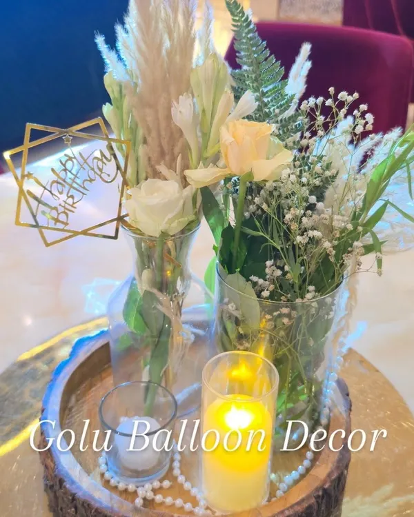An elegant boho-style table centerpiece featuring fresh flowers, pampas grass, and candles on a rustic wooden platter.