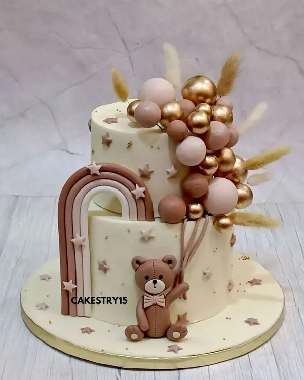 A sophisticated two-tier teddy bear cake for a baby celebration. This 2kg chocolate cake features a fondant teddy holding a cascade of pink and gold decorative balloons.