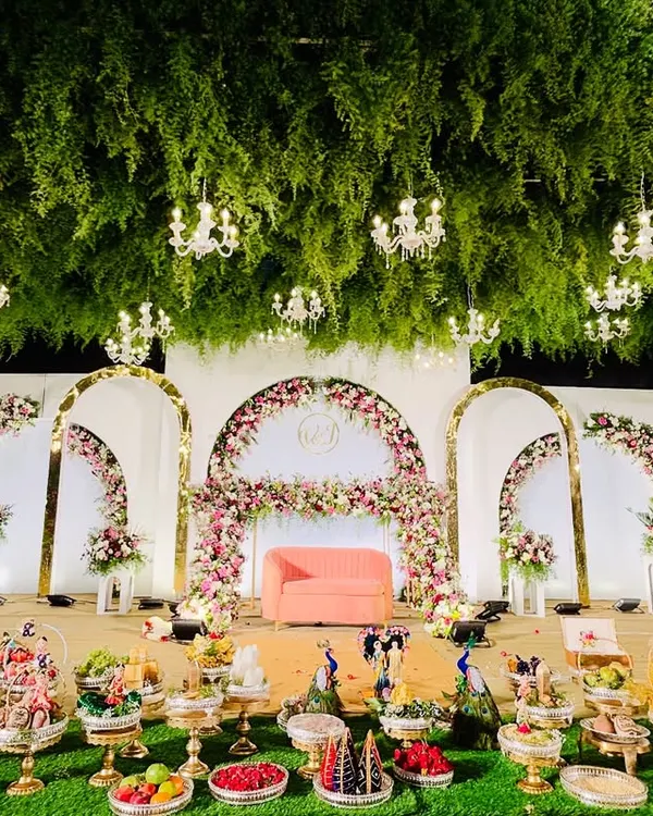 A stunning reception stage featuring a ceiling of lush greenery and dozens of hanging crystal chandeliers. This design creates an immersive, enchanted forest ambiance for an unforgettable evening.