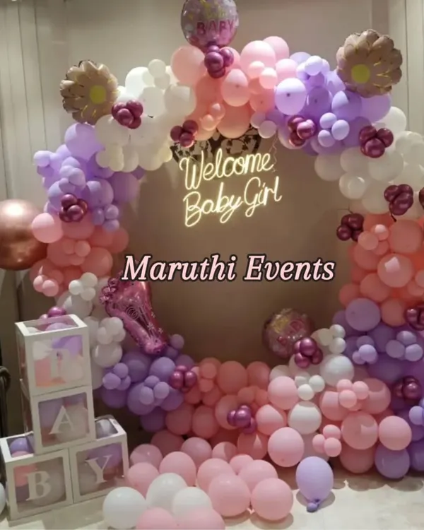 A beautiful "Welcome Baby Girl" shower. This circular balloon arch in pastel pink, purple, and white includes a neon sign and clear "BABY" blocks for a modern and sweet look.