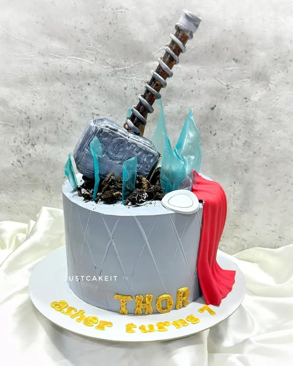 This Thor-themed cake is worthy of an Avenger, with an entirely edible Mjolnir hammer, sugar glass shards, and a flowing red cape. The details are crafted to look realistic and powerful.