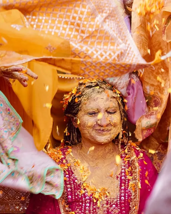 A blissful moment during the Haldi ceremony as the bride is covered in turmeric paste and flower petals under a traditional cloth. This image is full of color, texture, and pure happiness.