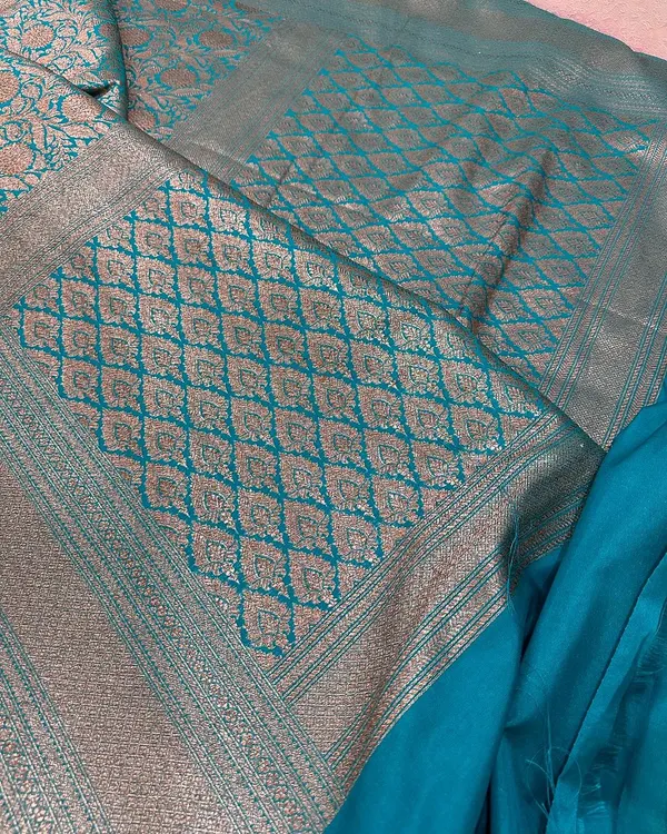 A complete look at this beautiful teal blue Banarasi silk saree. The rich pallu features a diamond-patterned jaal weaving in antique gold zari.