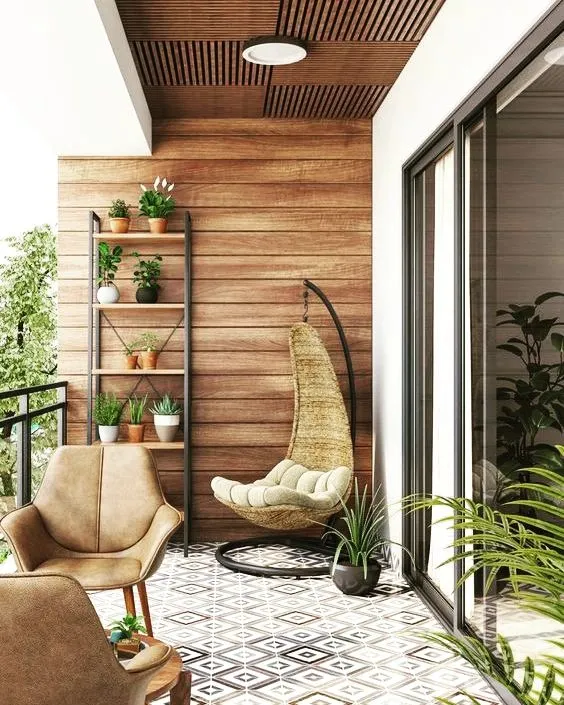 This cozy balcony is designed for relaxation, featuring a comfortable swing chair, a modern armchair, and a plant ladder to display greenery. The combination of a wood-paneled wall and patterned floor tiles adds warmth and character.