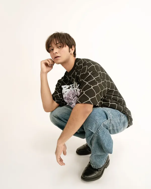 A clean, full-length shot for a streetwear brand's lookbook. The simple pose and direct lighting ensure the focus remains on the graphic t-shirt and baggy jeans.