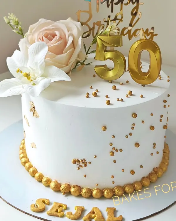 A beautiful cake for a 50th birthday, decorated with fresh flowers, gold sprinkles, and elegant gold numbers. The white and gold color scheme creates a classic and sophisticated look.