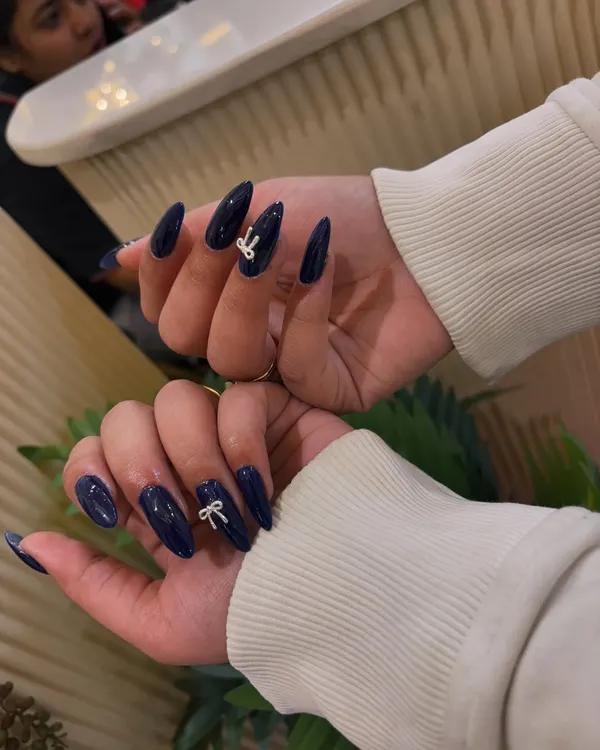 A simple yet chic design. We've elevated these glossy, deep blue almond-shaped nails by adding a delicate, white 3D bow accent.
