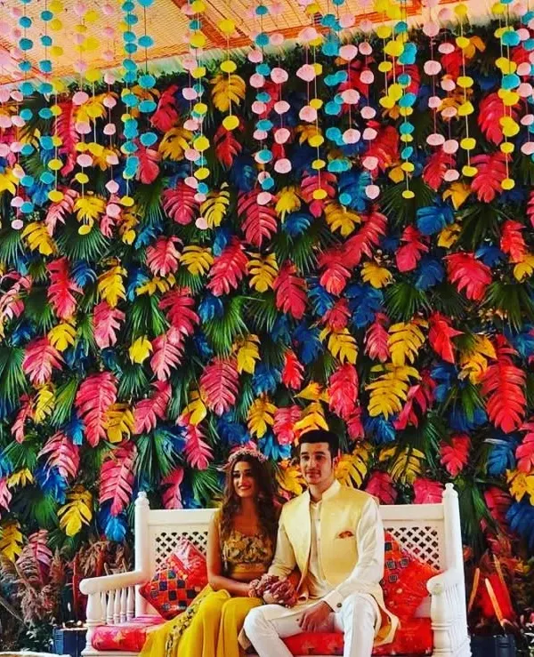 A vibrant and unique photo backdrop created with a wall of multi-colored leaves. We provide complete seating arrangements, like this white bench with custom cushions, to perfectly match your chosen theme.
