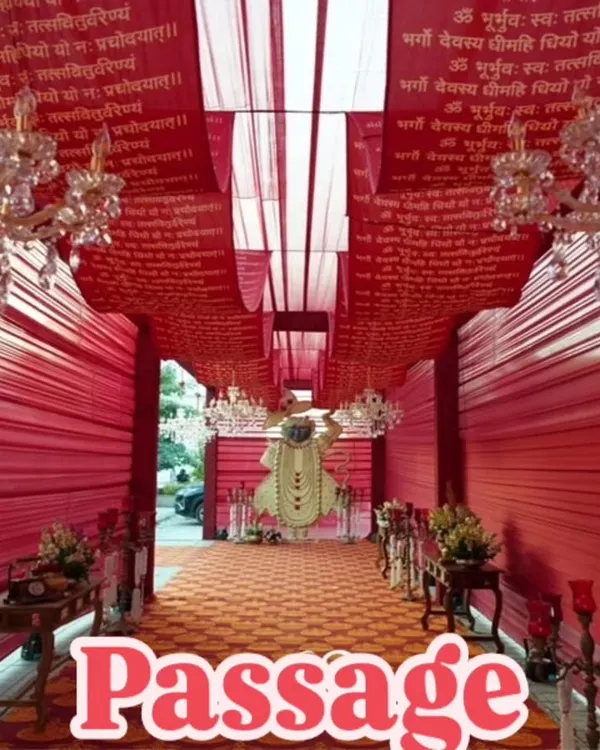This grand passage is designed for a traditional ceremony, draped entirely in red fabric printed with sacred mantras. The crystal chandeliers and a divine statue at the end create a deeply spiritual and opulent pathway.