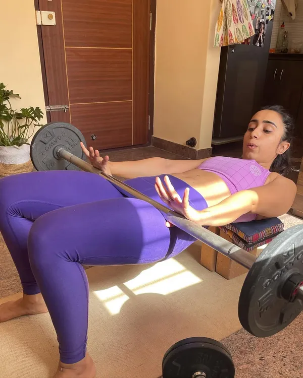 Performing a weighted hip thrust at home using a barbell. This shows how we can adapt key strength exercises for an effective at-home workout.