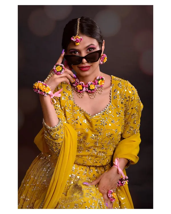 A modern and playful take on a traditional look. The model wears a stunning yellow lehenga and floral jewelry, but adds a pair of sunglasses for a touch of contemporary cool.