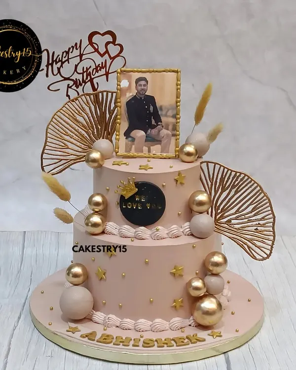 A personalized two-tier butterscotch cake for a special birthday. This elegant design features an edible photo frame, golden decorative balls, and delicate dried fern accents.
