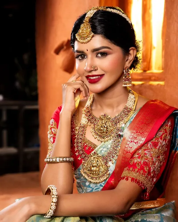A classic South Indian bridal portrait. The makeup features a bold red lip, defined eyes, and glowing skin, perfectly complementing the traditional temple jewelry and silk saree.