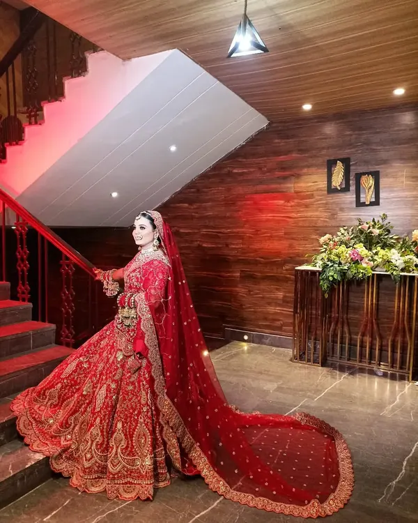 A stunning bridal portrait in a royal red lehenga with a long trail, captured on a staircase to emphasize its grandeur.