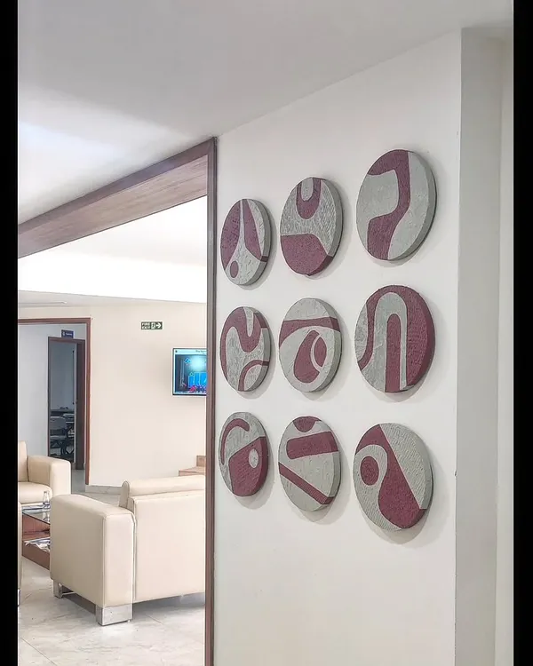This custom art installation features a set of nine circular, textured panels. The abstract maroon patterns on the grey, textured base create a striking 3D effect on the wall of this modern living space.