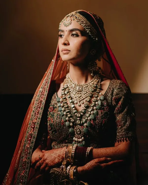 A breathtaking close-up of the bride in her royal attire, her gaze thoughtful and serene. The warm lighting highlights the intricate details of her jewelry and outfit.
