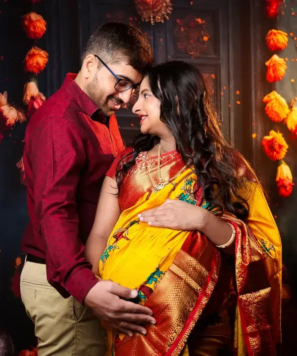 A beautiful moment between a couple during their traditional maternity shoot. The warm glow from the diyas and marigold decor perfectly complements the rich colors of their ethnic attire.