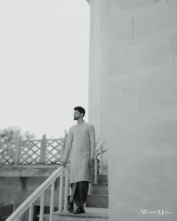 A stylish black and white portrait of the groom in his traditional attire. The architectural background and his confident pose create a modern yet timeless look.