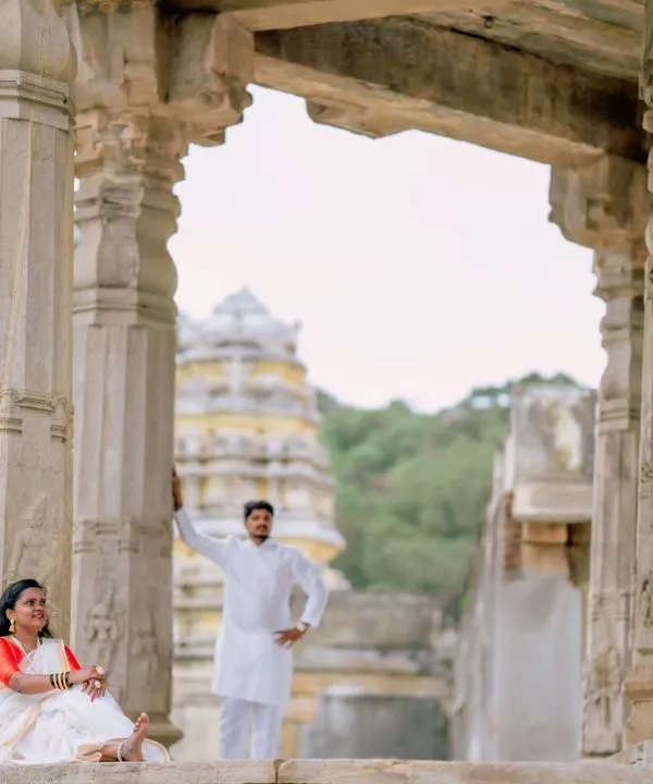 A wide shot of a couple posing amidst the stone pillars of a historic temple, with the gopuram visible in the background. This composition emphasizes the grandeur of the location.