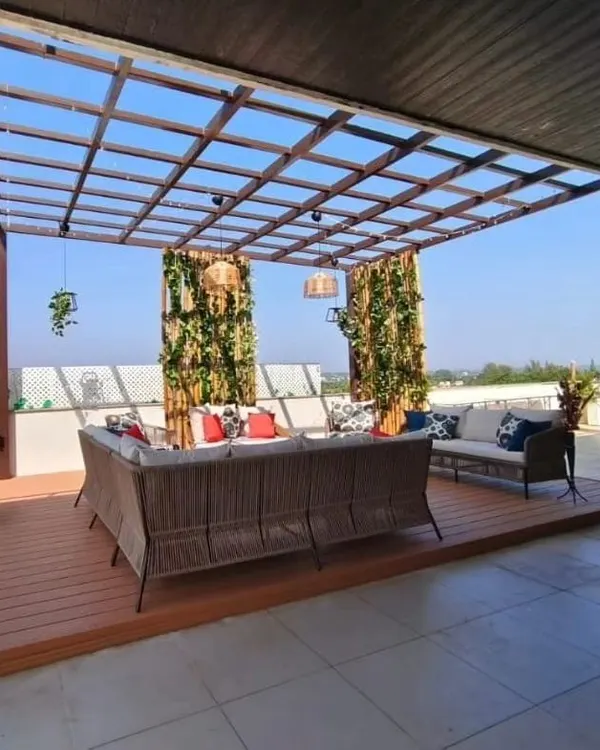 A wide-angle view of a spacious terrace pergola designed for Rishab Girias, Director of Girias Electronics. This structure features a powder-coated MS frame, a glass top, and a durable WPC deck, creating an expansive and stylish lounge area.
