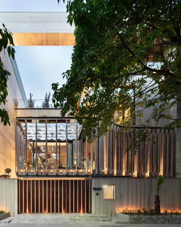 The facade of our Punjabi Bagh residence, seen here at dusk, highlights the dialogue between solid and void. The illuminated glass box, shielded by a wooden screen, establishes a strong connection between the interior and the mature trees outside.