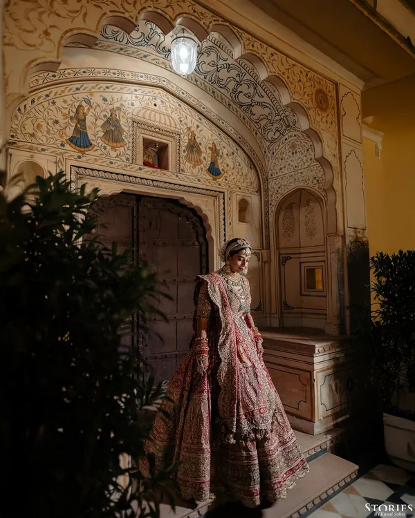 A stunning portrait of the bride, Aashi, standing in a beautifully lit archway at Mundota Palace, capturing the grandeur and solitude before the ceremony begins.