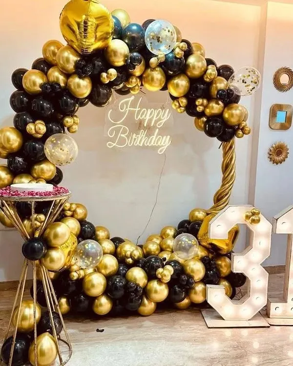 A stunning black and gold heart-shaped balloon arch for a 31st birthday. This setup includes a cake stand, a "Happy Birthday" neon sign, and large marquee numbers, creating a glamorous photo corner.