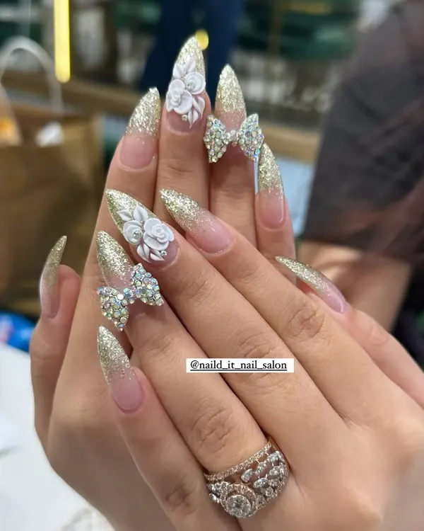Our signature festive look, perfect for Karwachauth or your wedding day. This design features long stiletto extensions with a sparkling gold glitter base, intricate 3D acrylic roses, and fully crystallized Swarovski bows for maximum drama.