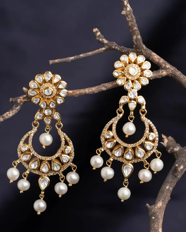 These stunning chandbali earrings are crafted with a floral stud and a crescent moon drop, both adorned with kundan-style stones and pearls. They are the epitome of royal elegance.