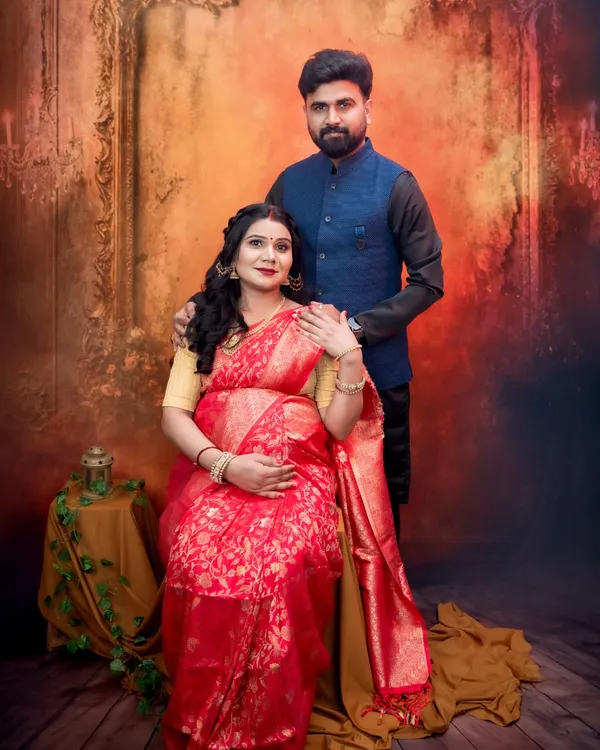 A proud portrait of a couple celebrating their Maharashtrian roots. The rich red saree, the groom's traditional jacket, and the classic studio backdrop come together beautifully.